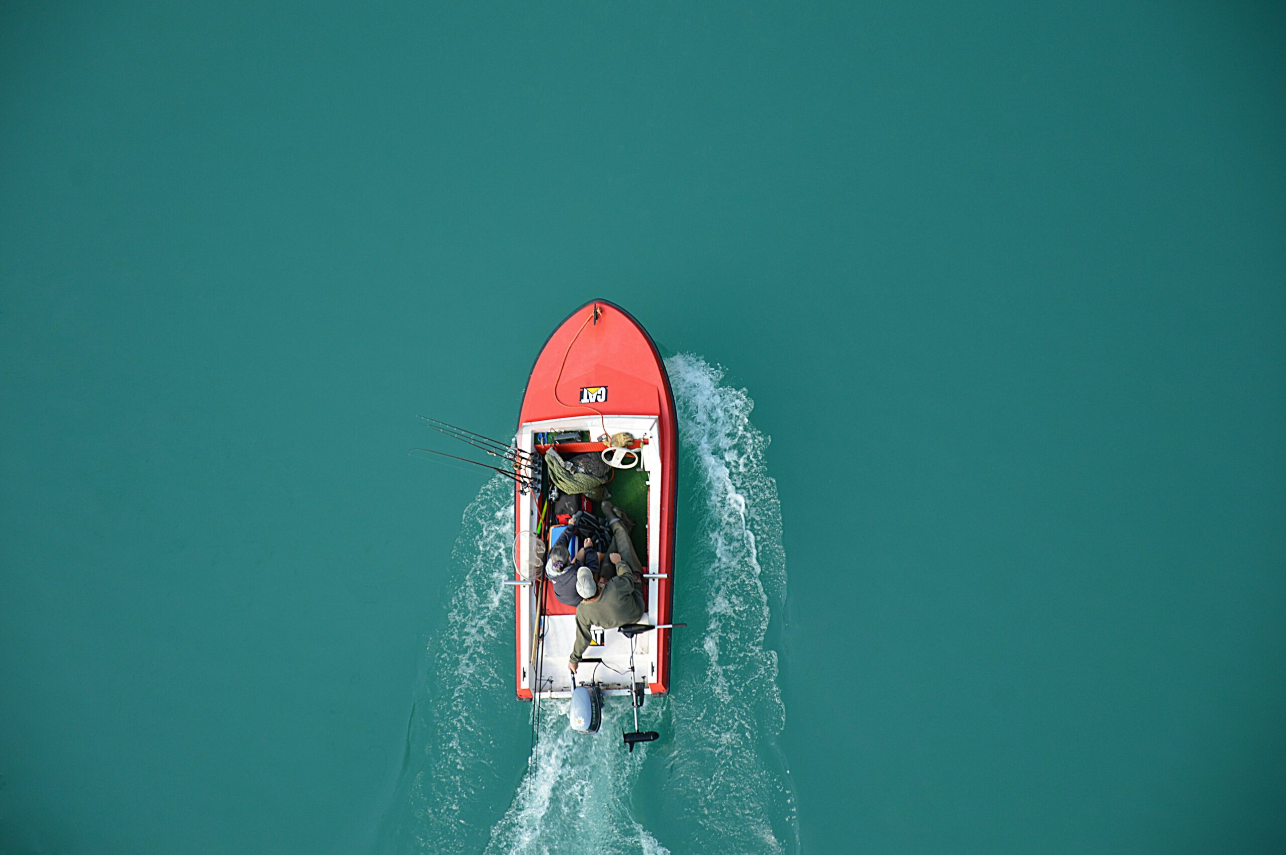 Top view of a red motorboat with fishermen navigating open turquoise waters.