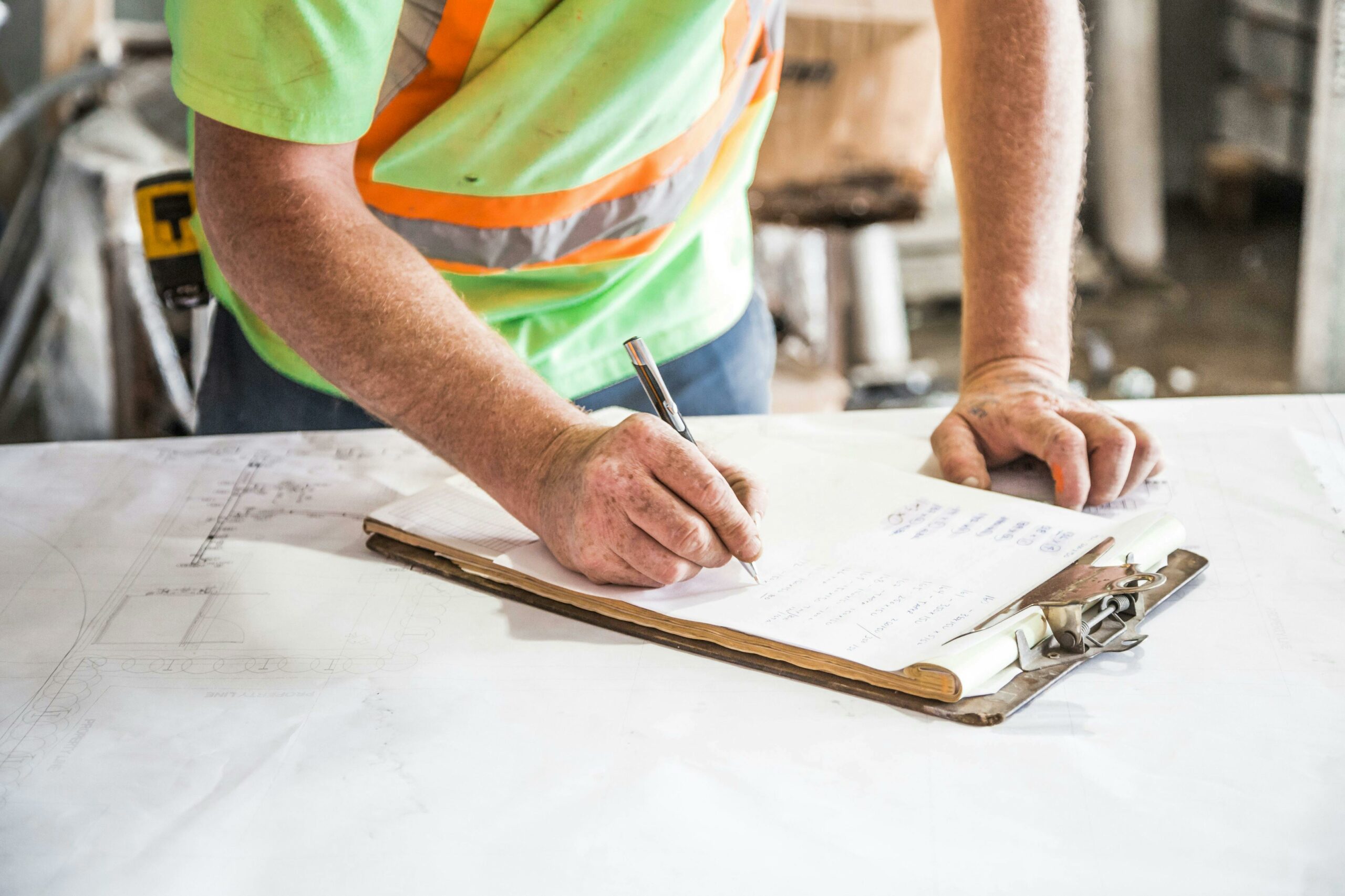 A construction worker writes notes on a clipboard at a construction site, emphasizing planning and precision.